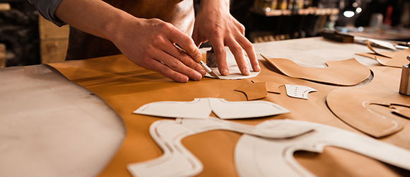 a leathermaker using stencils to cut out leather pieces on a worktop 